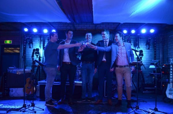 Vijf collega’s proosten samen op een podium tijdens een feest.